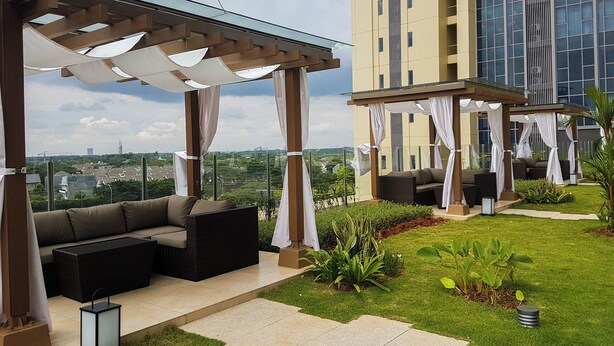 A rooftop patio with outdoor seating, a glass pergola, and a view of a cityscape.