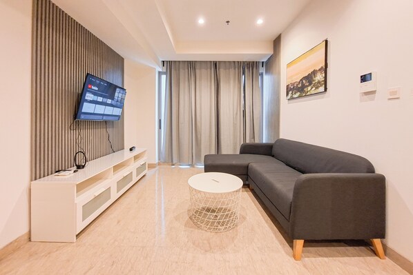 Un salon moderne avec un canapé gris, un téléviseur blanc fixé au mur, une console blanche et une table basse ronde.