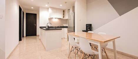A modern kitchen with a central island, white cabinetry, and a dining area with a wooden table and chairs.