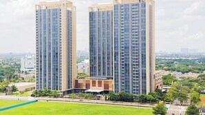 A high-rise residential building with multiple floors, surrounded by greenery and a clear sky.