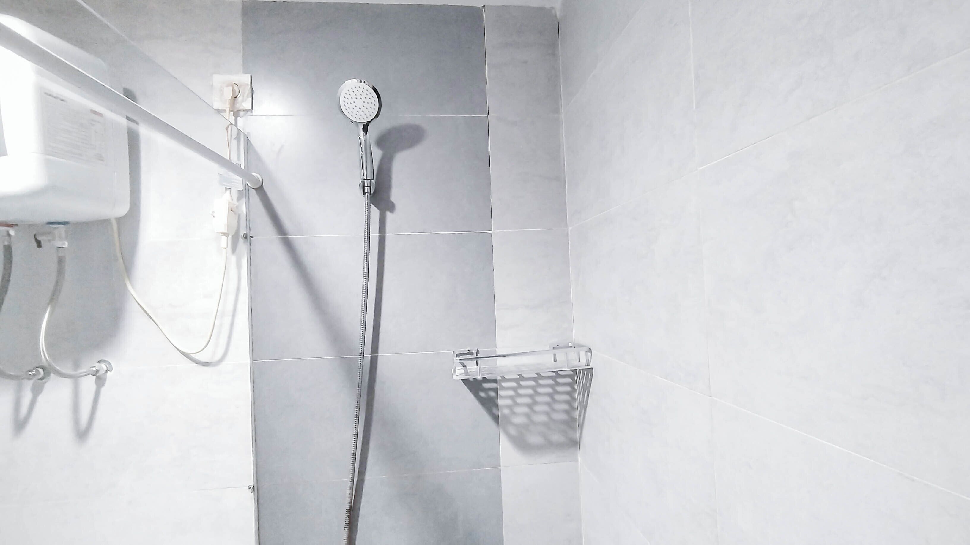 Une salle de bain avec des carreaux blancs, une pomme de douche, un pommeau de douche amovible et un porte-savon à suspendre dans la douche.