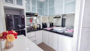 Una cocina moderna con armarios blancos, un refrigerador negro, una cafetera y un lavamanos.