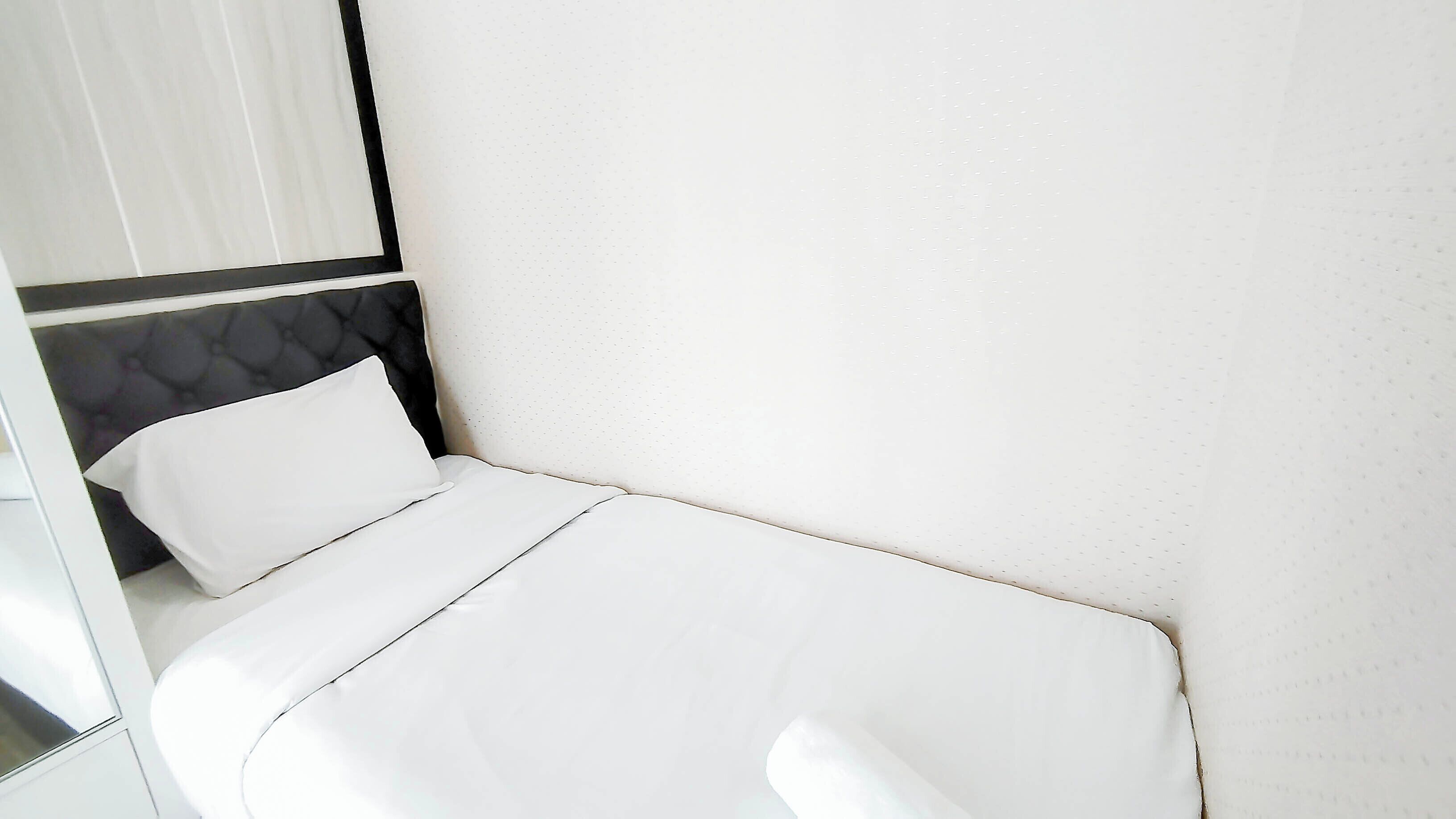 A small, neatly made bed with white linens in a room with a simple, modern design.