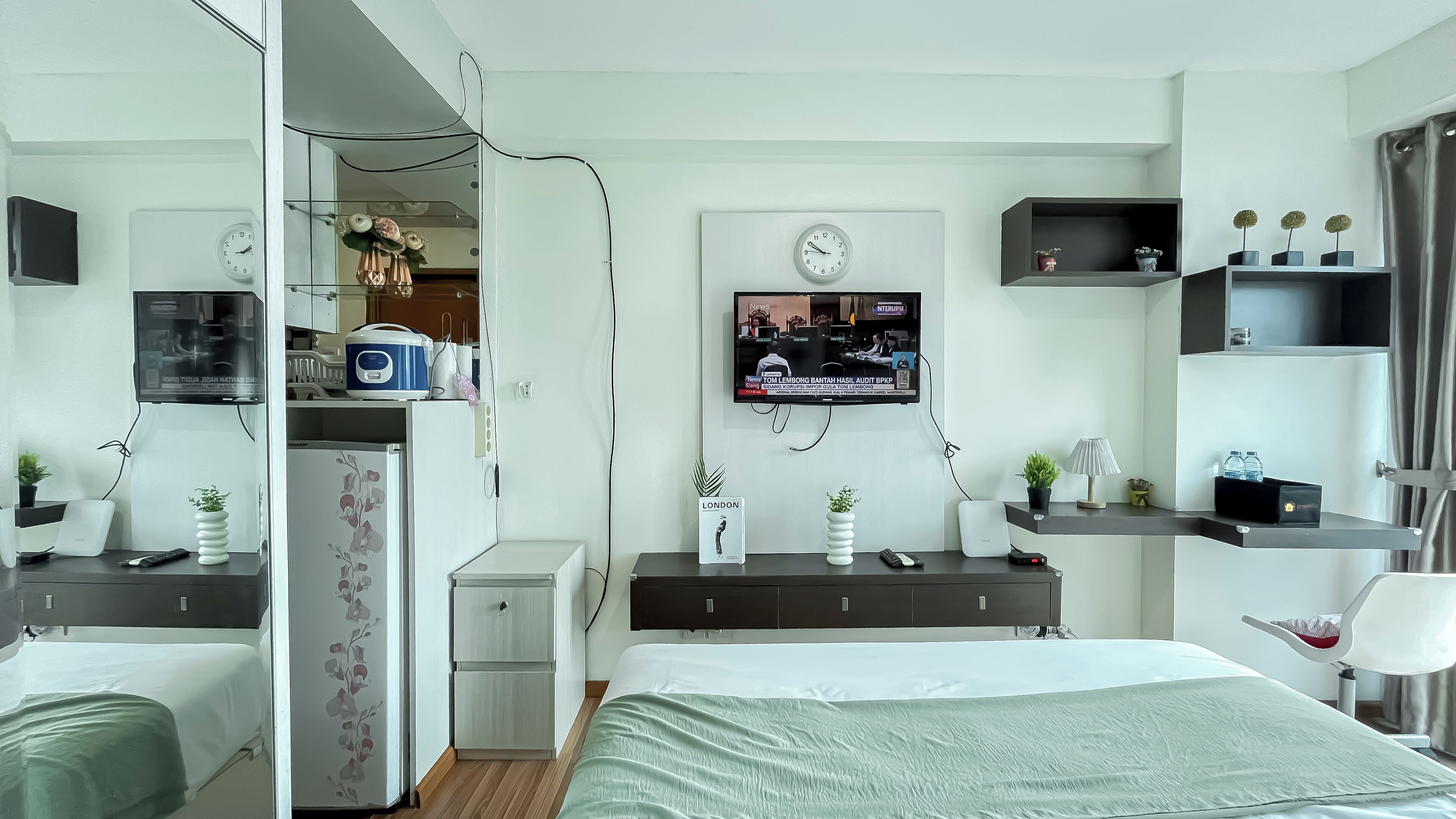 Habitació d'hotel moderna amb un llit, una taula de treball, una televisió i una cuineta petita.
