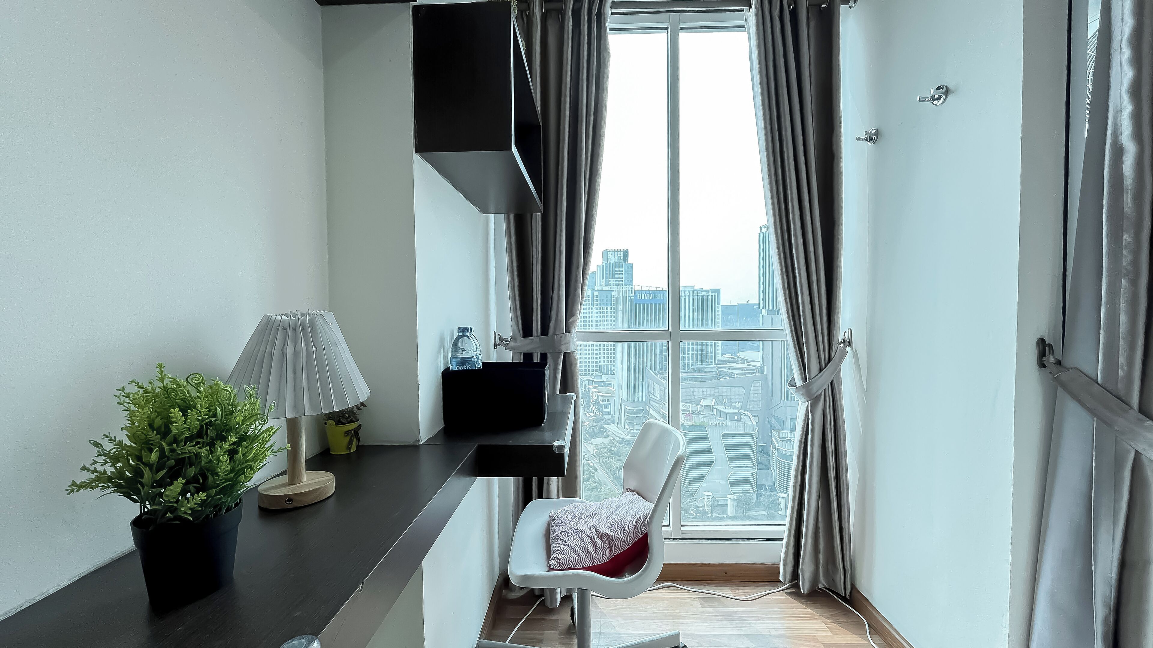 A modern apartment with a large window, a white chair, a small table, and a potted plant.