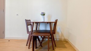 A dining area with a wooden table and four chairs, a vase with flowers, and a door to the left. - Warm And Cozy 1Br With Makeup Room At Meikarta Apartment (Cikarang)