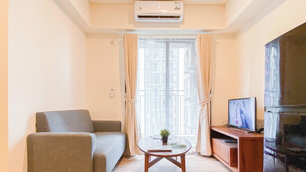 A living room with a sofa, a coffee table with a plant, a television, and an air conditioning unit. - Warm And Cozy 1Br With Makeup Room At Meikarta Apartment (Cikarang)