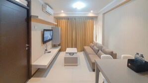 Una habitación de hotel moderna con sofá, televisor montado en la pared, escritorio con ordenador y ventana con cortinas.