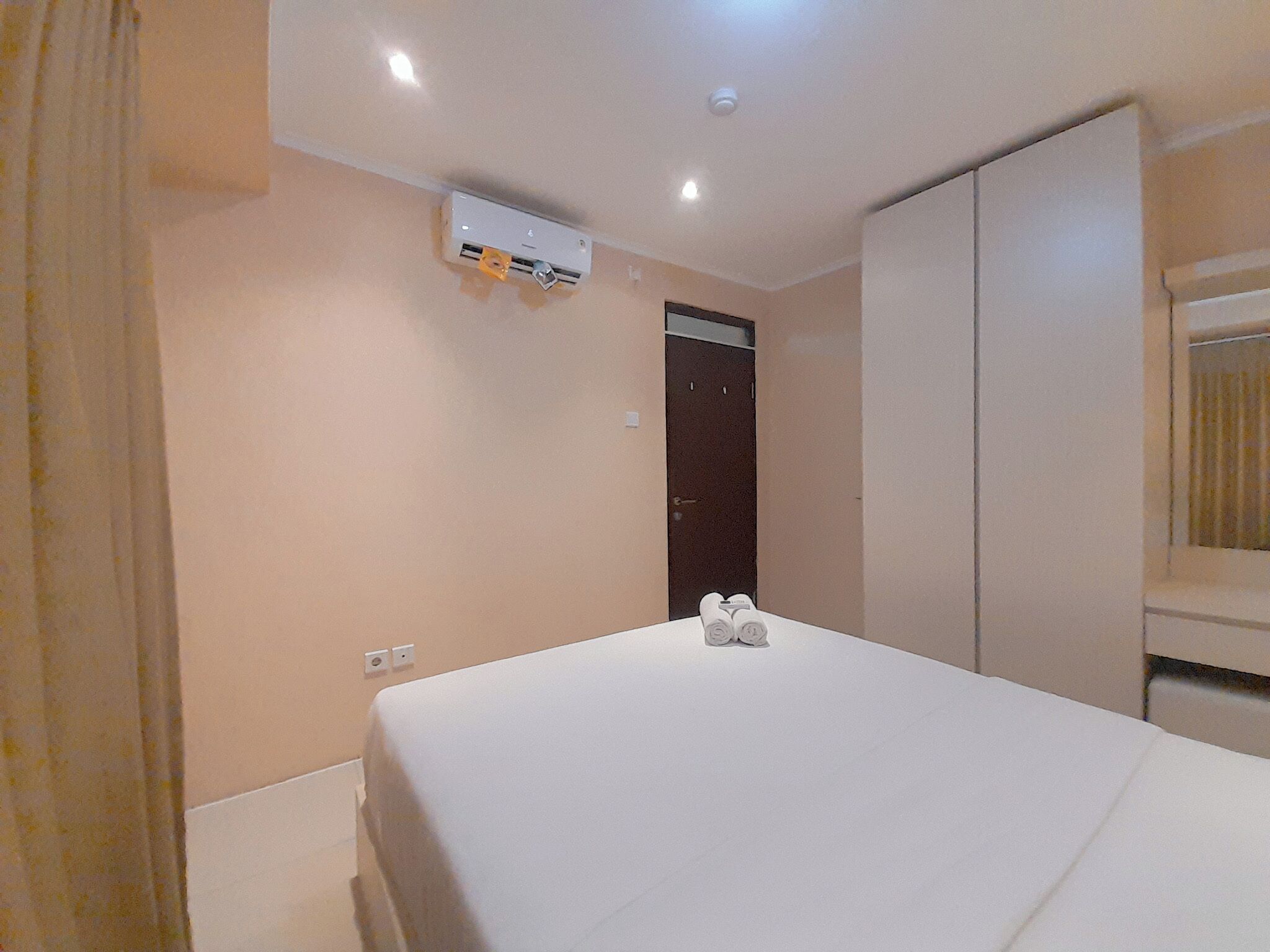 A hotel room with a bed, an air conditioning unit, a wardrobe, and a door.