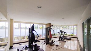Un gimnasio con equipo de ejercicio, amplias ventanas y vistas a un cuerpo de agua.
