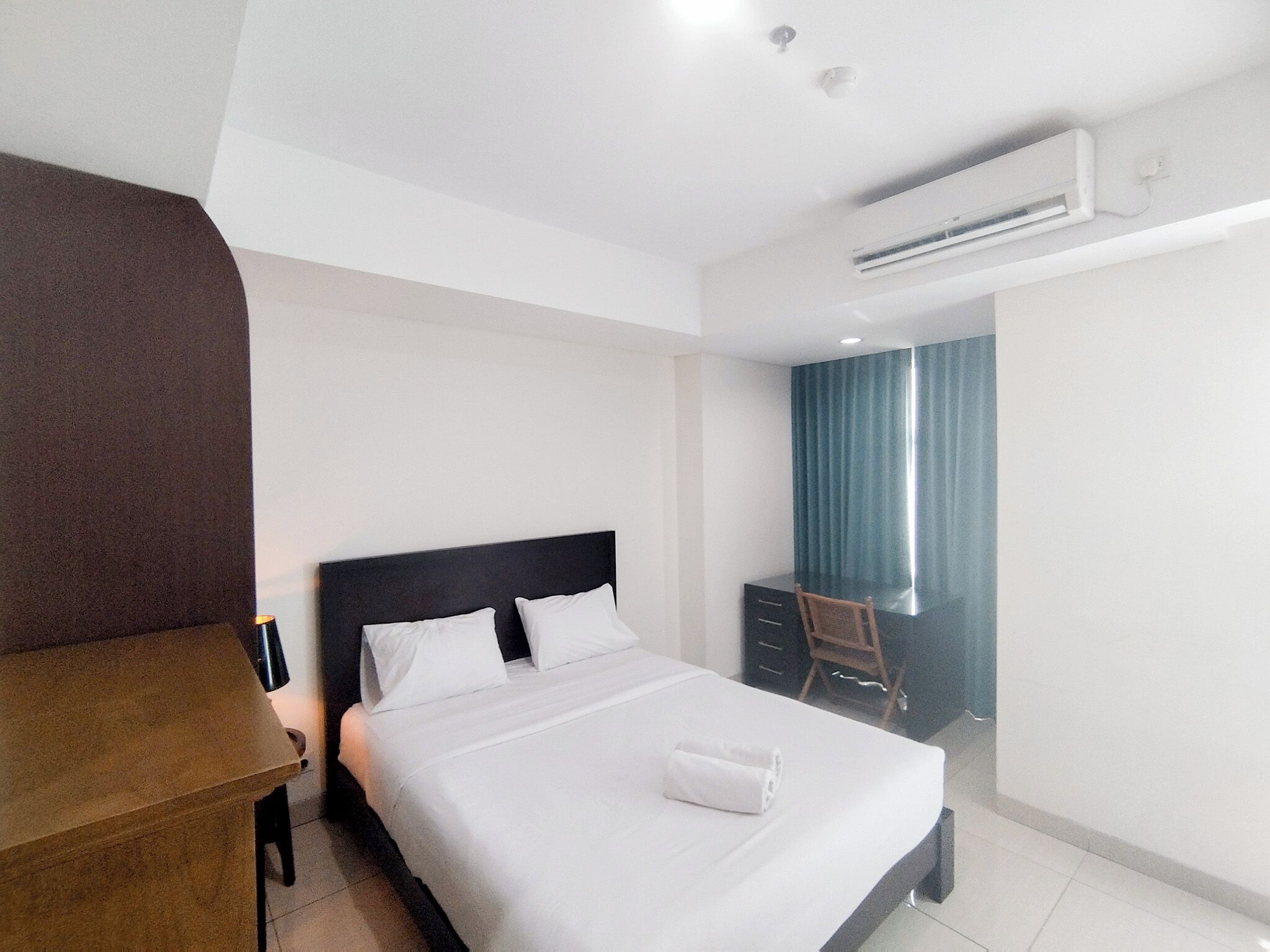 A hotel room with a bed, a desk, a chair, and an air conditioning unit.
