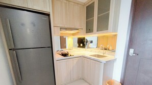 A compact kitchen with a refrigerator, sink, and wooden cabinets. - Spacious Studio Room At Grand Sungkono Lagoon Apartment (Surabaya)