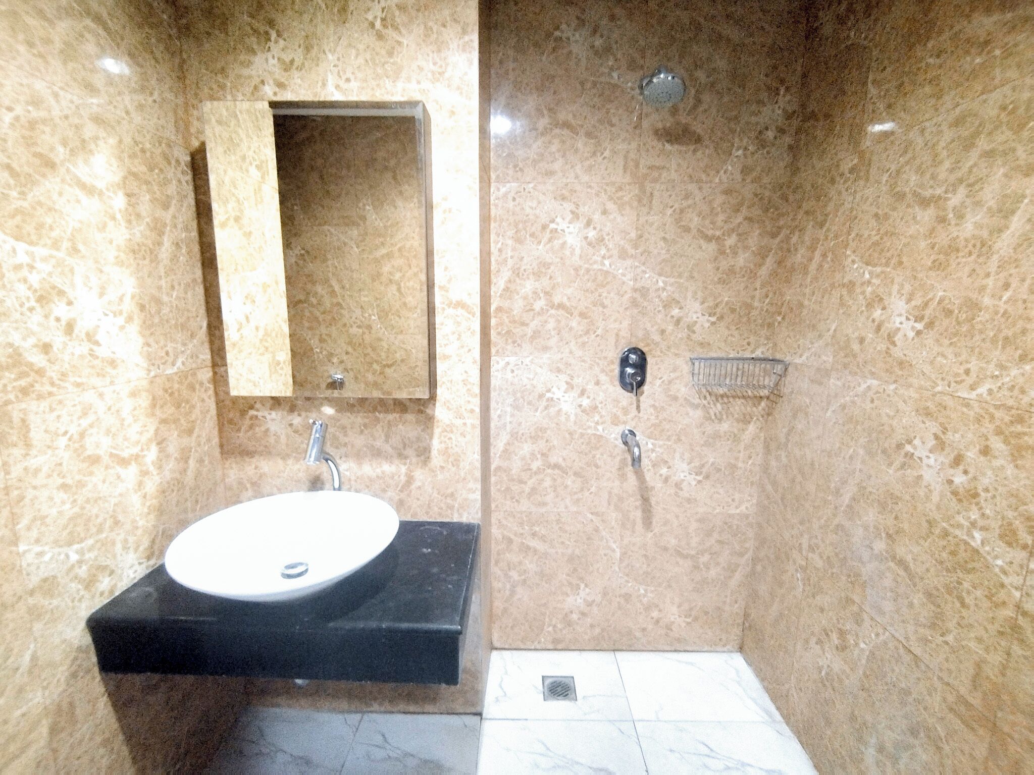 Un baño con lavamanos de mármol, un espejo, ducha y toallero.