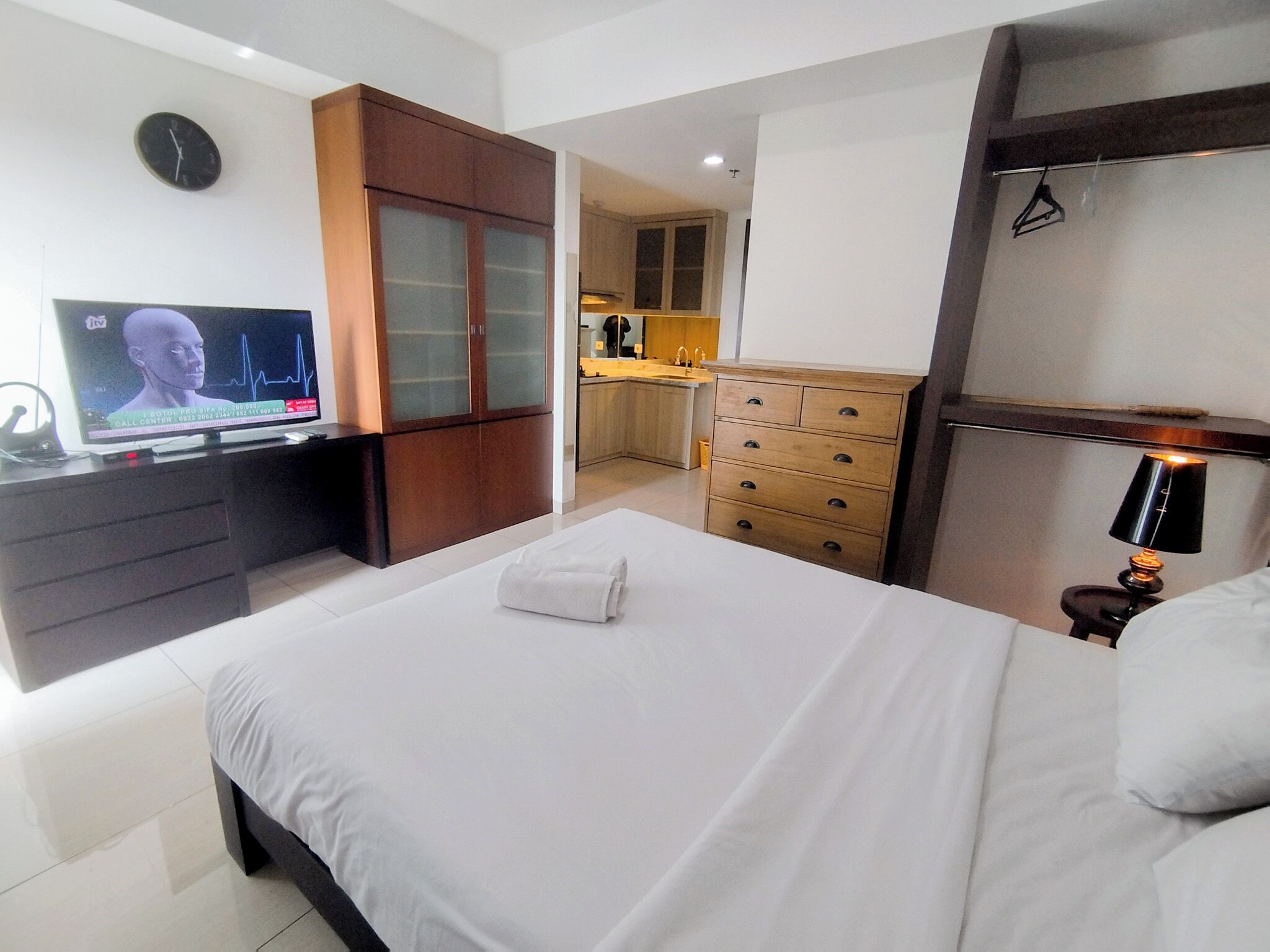 A hotel room with a bed, a TV, a wooden wardrobe, a kitchen area, and a bathroom.