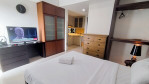 A hotel room with a bed, a TV, a wooden wardrobe, a kitchen area, and a bathroom. - Spacious Studio Room At Grand Sungkono Lagoon Apartment (Surabaya)