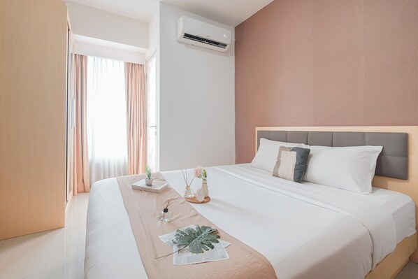 A neatly made bed with a headboard, a bedside table with a plant, and a window with curtains. - Simple 1Br Without Living Room At Grand Kamala Lagoon Apartment (Bekasi)