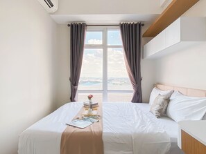 A hotel room with a bed, a bedside table, and a window with curtains. - Neat 1Br At Vasanta Innopark Apartment (Cikarang)