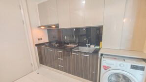 A modern kitchen with dark cabinetry, a built-in sink, and a front-loading washing machine. - Warm 3Br Direct Access To Mall La Riz Supermall Mansion Apartment (Surabaya)