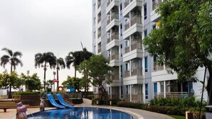 A residential building with a swimming pool, slides, and palm trees. - Warm 3Br Direct Access To Mall La Riz Supermall Mansion Apartment (Surabaya)
