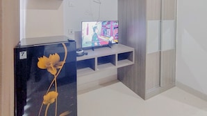 A modern living room with a flat-screen TV on a white stand, a black refrigerator with a floral design, and a wooden cabinet. - Simply Design Studio At Taman Melati Surabaya Apartment (Surabaya)