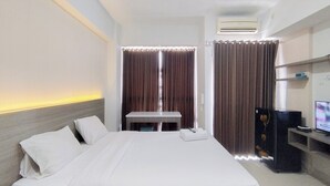 A hotel room with a bed, a small table, a TV, and a refrigerator. - Simply Design Studio At Taman Melati Surabaya Apartment (Surabaya)