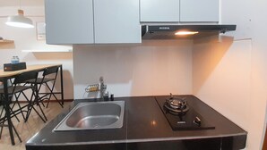 Une cuisine de taille réduite, dotée d’un plan de travail noir, d’un évier en acier inoxydable et d’une cuisinière à gaz.