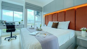 Een moderne hotelkamer met een groot bed, een bureau met stoel, en uitzicht op de stad door grote ramen.