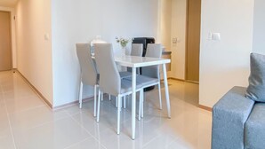 A modern dining area with a white table and four grey chairs, a vase with flowers, and a coffee machine. - Modern Style 2Br Apartment At Meikarta (Cikarang)