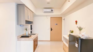 A modern kitchen with a built-in stove, a sink, and a refrigerator. There is a door with a sign on it and a small plant on the counter. - Simple Look 2Br Apartment Meikarta (Cikarang)