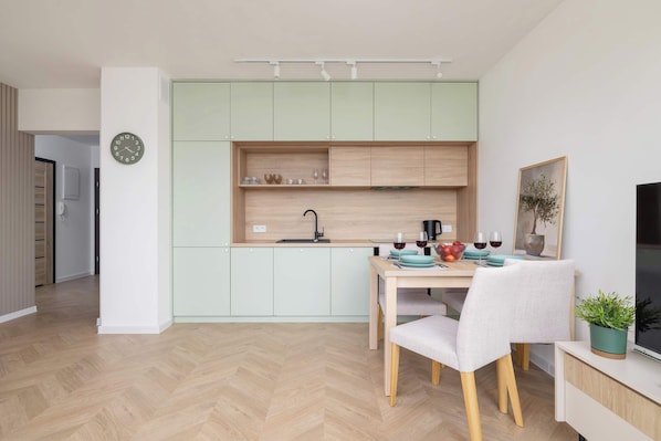 A modern kitchen with light green cabinets, a wooden countertop, and a dining area with a table and chairs.