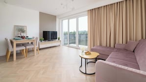 Uma sala de estar moderna com sofá, mesa de jantar com cadeiras, televisão e uma janela grande com cortinas.