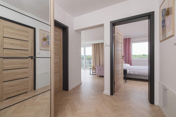 A hallway with a mirrored wardrobe and wooden floors leading into a bedroom.