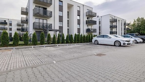 Um edifício residencial moderno com vários andares, varandas, estacionamento pavimentado e sebes bem aparadas.