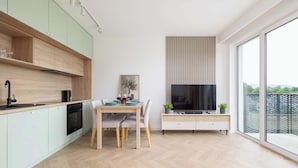 Uma cozinha moderna com armários de madeira clara, uma área de jantar com mesa e cadeiras, TV embutida e uma grande janela com vista para o exterior.