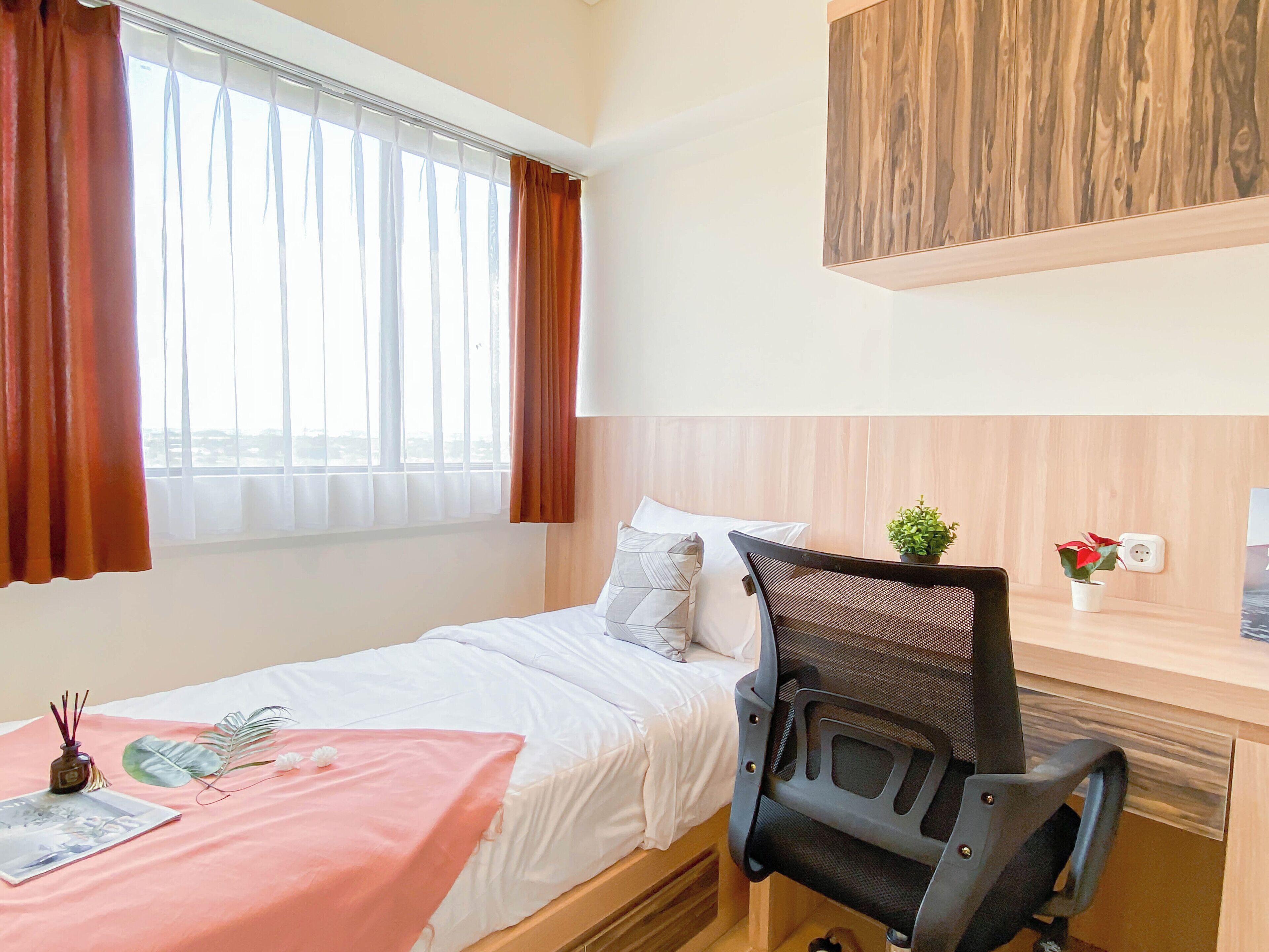 A bedroom with a single bed, a desk, a chair, and a window with curtains.