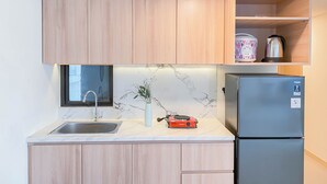 Una cocina compacta con armarios de madera, un protector contra salpicaduras de mármol, un lavamanos, un hervidor y un refrigerador.
