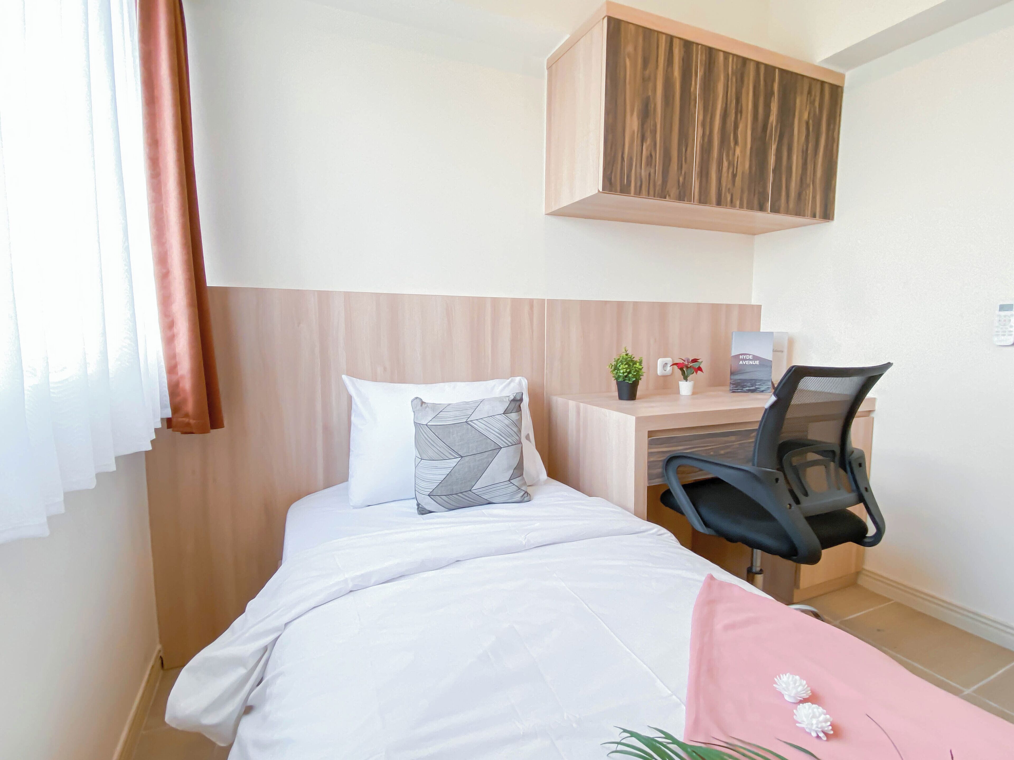 A hotel room with a bed, a desk, a chair, a wooden headboard, and a small potted plant.
