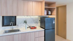 Una cocina compacta con armarios de madera, encimera de mármol, un lavabo, un refrigerador negro y una tetera en la estantería.