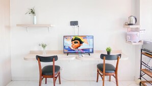 A small kitchenette with a TV, two chairs, a shelf with a plant, and a kettle. - Simple Studio (No Kitchen) Near President University At Elvis Tower Apartment (Cikarang)