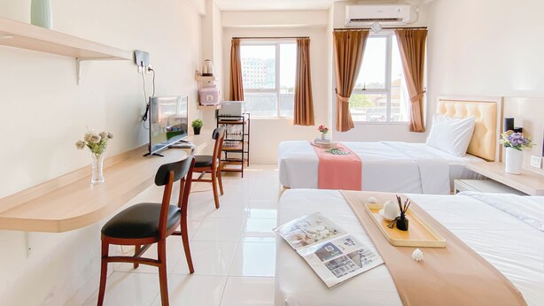 A hotel room with a desk, two beds, a TV, and a window with curtains. - Simple Studio (No Kitchen) Near President University At Elvis Tower Apartment (Cikarang)