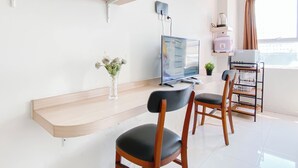 A modern room with a wooden desk, two black chairs, a flat-screen TV, a small potted plant, and a window with curtains. - Simple Studio (No Kitchen) Near President University At Elvis Tower Apartment (Cikarang)