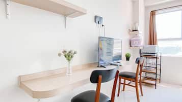 A modern room with a wooden desk, two black chairs, a flat-screen TV, a small potted plant, and a window with curtains.
