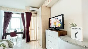 A modern living room with a TV, a Sharp refrigerator, a bookshelf, and a window with curtains. - Studio Apartment Near Kebayoran Station At Pakubuwono Terrace (Jakarta)