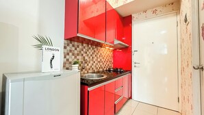 A kitchen with red cabinets, a white door, and a tiled backsplash. - Studio Apartment Near Kebayoran Station At Pakubuwono Terrace (Jakarta)
