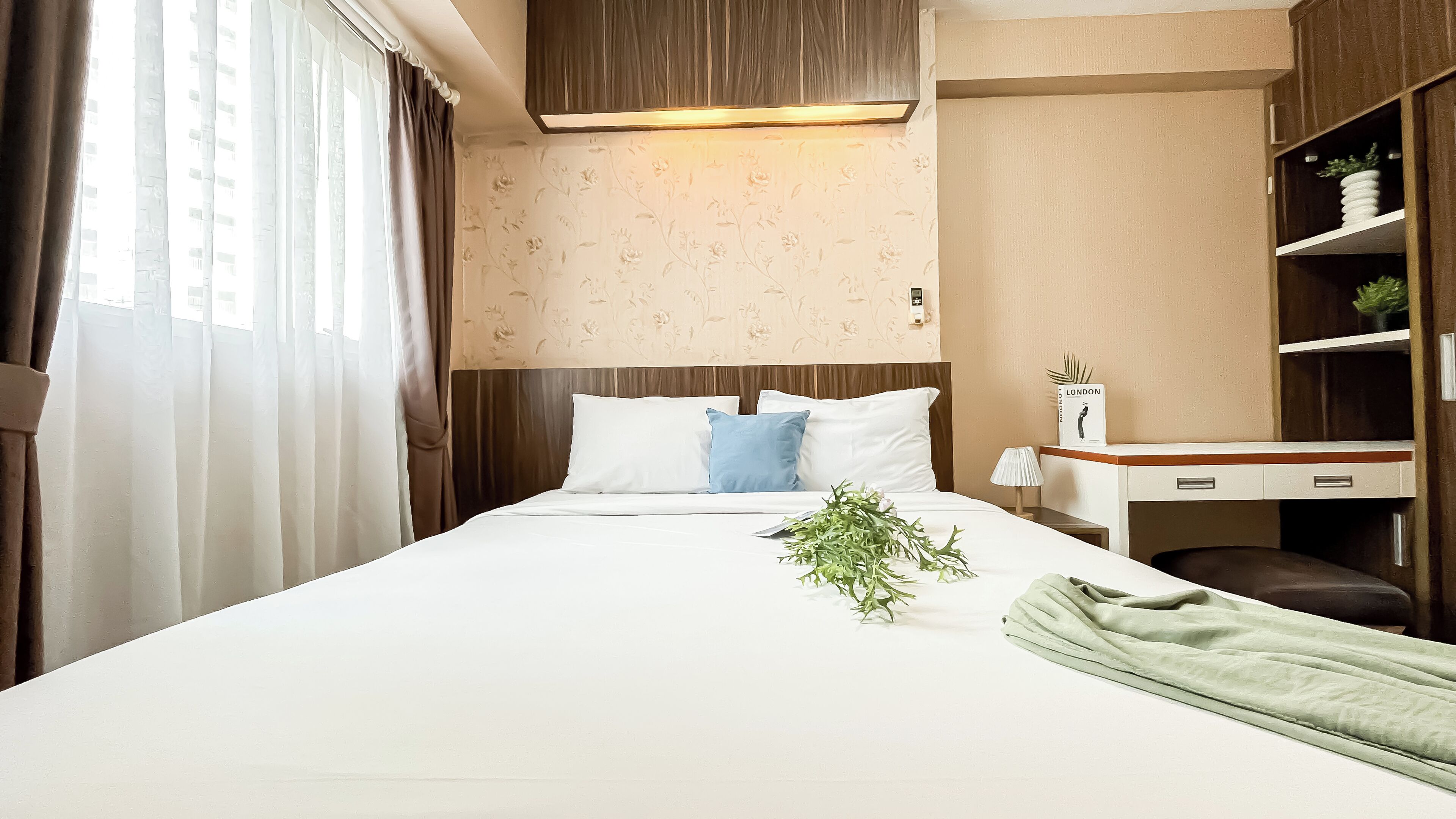 A hotel room with a bed, a desk, a chair, and a bookshelf.
