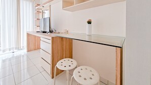 A modern kitchen with a glass countertop, wooden cabinets, and two white stools.