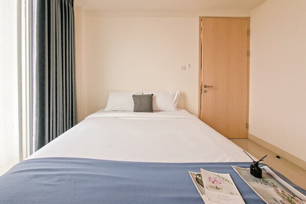 A hotel room with a bed, a wooden door, and a window with curtains.