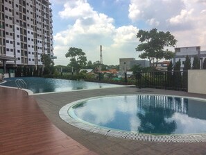 A rooftop swimming pool with a wooden deck and a view of surrounding buildings. - Urban Modern Studio Apartment Oasis Cikarang (Cikarang)