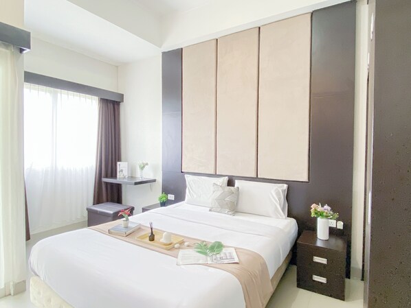 A modern hotel room with a large bed, a bedside table, a nightstand, and a wardrobe. - Urban Modern Studio Apartment Oasis Cikarang (Cikarang)