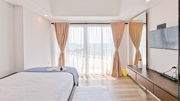 A modern hotel room with a large bed, a bench, a TV, and a balcony view. - Comfy Rustic Studio Apartment At Casa De Parco (Pagedangan)